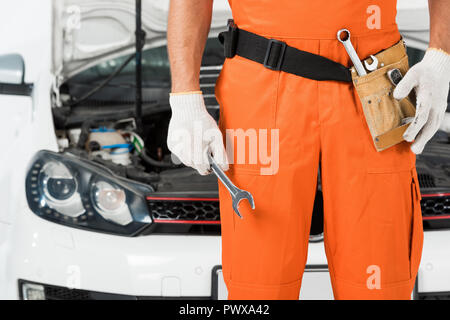 cropped image of auto mechanic holding wrench near car on white Stock Photo