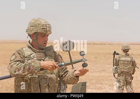 U.S. Air Force Master Sgt. Scott Hose, the NCOIC of weather assigned to the 370th Air Expeditionary Advisory Group, Detachment 1, conducts a preventative maintenance inspection on a weather sensor while Master Sgt. Shannon Hawkins performs security of the area at Qayyarah West Airfield, Iraq, July 2, 2017. Scott and his brother Master Sgt. Daniel Hose are both deployed to Iraq in support of Combined Joint Task Force -Operation Inherent Resolve. CJTF-OIR is the global Coalition to defeat ISIS in Iraq and Syria. Stock Photo