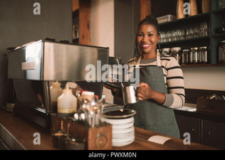 Smiling young African barista preparing coffee behind a cafe counter Stock Photo