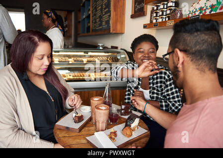 Smiling friends sitting at a cafe table eating desserts together Stock Photo