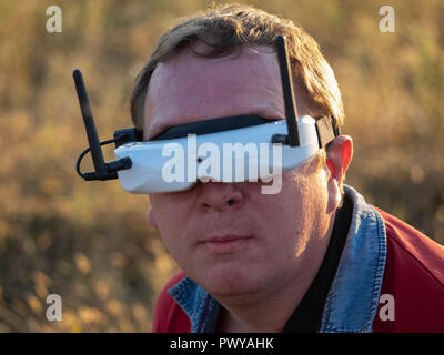 Drone pilot seen wearing a first-person view headset. Young man driving a quad-copter using video-goggles. Stock Photo