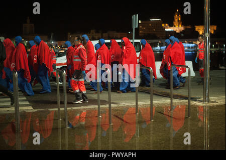 Migrants covered with red blankets are seen walking on the promenade as they are reflected in the water after they disembark from a rescue vessel at the Port of Malaga. Spain’s Maritime Rescue service rescued 146 migrants from three dinghies at the Alboran Sea and brought them to Malaga Harbour, where they were assisted by the Spanish Red Cross. Stock Photo