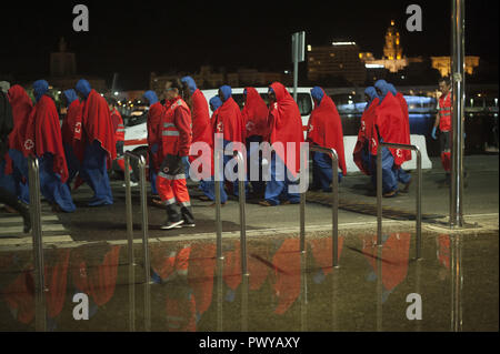 Malaga, Spain. 19th Oct, 2018. Migrants covered with red blankets are seen walking on the promenade as they are reflected in the water after they disembark from a rescue vessel at the Port of Malaga. Spain's Maritime Rescue service rescued 146 migrants from three dinghies at the Alboran Sea and brought them to Malaga Harbour, where they were assisted by the Spanish Red Cross. Credit: Jesus Merida/SOPA Images/ZUMA Wire/Alamy Live News Stock Photo