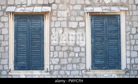 Two windows in old wall with closed blue shutters Stock Photo