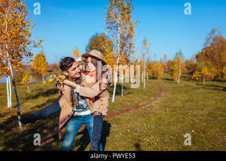 Young couple walks in autumn forest. Man giving his girlfriend piggyback. People having fun outdoors Stock Photo