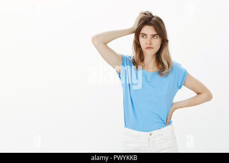 Girl facing problem, thinking how solve it. Focused troubled attractive young woman with fair hair, scratching head, holding hand on hip and looking aside with serious face, trying to find solution Stock Photo