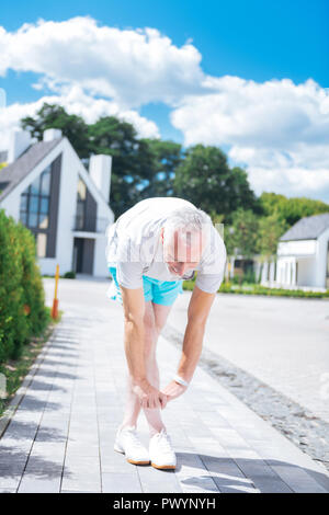 Grey-haired businessman stretching his body after doing morning exercises Stock Photo