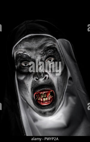 closeup of a frightening evil nun, with bloody teeth and scary eyes, wearing a typical black and white habit, emerging from the dark Stock Photo