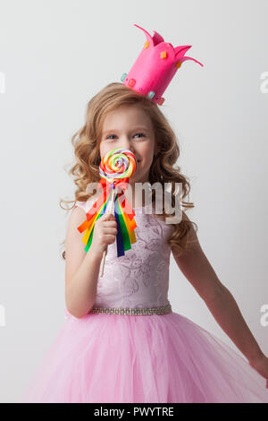 Beautiful little candy princess girl in crown holding big lollipop and smiling Stock Photo