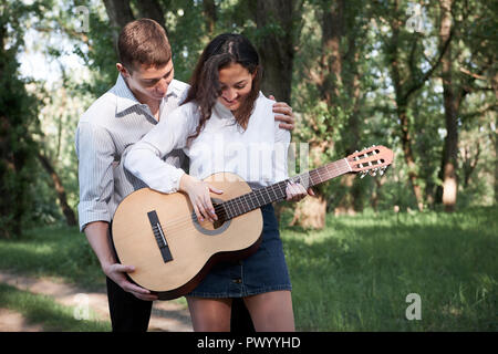 young couple walking in the forest, playing guitar and dancing, summer nature, bright sunlight, shadows and green leaves, romantic feelings Stock Photo