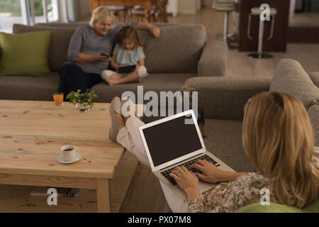 Woman using laptop while grandmother and granddaughter using mobile phone and digital tablet Stock Photo