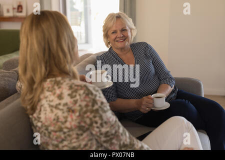 Mother and daughter interacting with each other while having coffee in living room Stock Photo