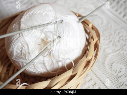 Woolen ball for knitting in the vintage wicker basket on the lace background. Cozy home activity concept. Stock Photo