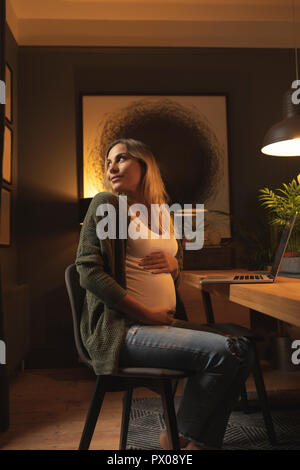 Pregnant woman looking behind while using laptop Stock Photo