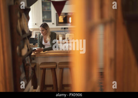 Pregnant woman texting on the phone in kitchen Stock Photo