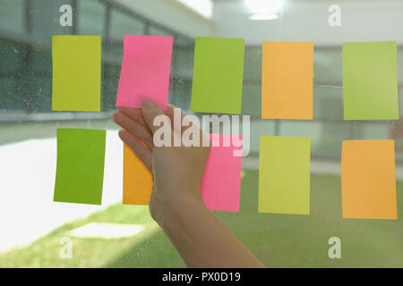hand hold adhesive notes on glass wall at workplace. Sticky note paper reminder schedule for creative idea & business brainstorming Stock Photo