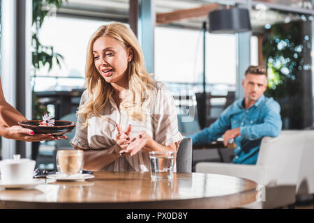 surprised blonde woman looking at dessert with flower in restaurant Stock Photo