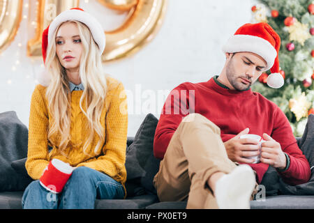 upset couple in bad mood holding cups of coffee and sitting at home on christmas eve Stock Photo