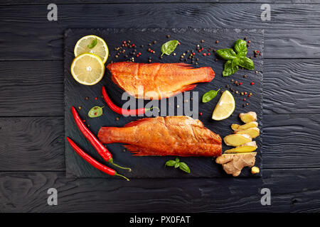 hot smoked red snappers on a black stone tray with spices, herbs and sliced lemons, view from above, flatlay Stock Photo