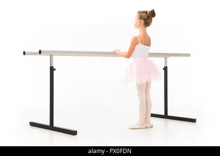 rear view of little ballerina in tutu and pointe shoes practicing at ballet barre stand isolated on white background Stock Photo