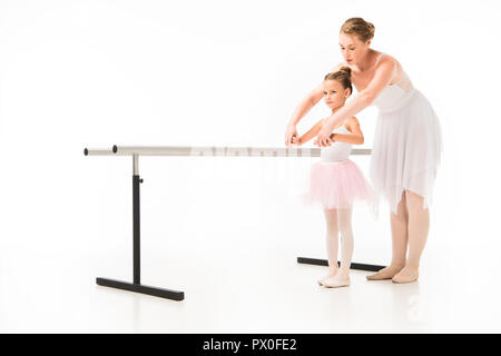 female teacher in tutu helping little ballerina practicing at ballet barre stand isolated on white background Stock Photo