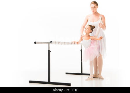 focused female teacher in tutu helping little ballerina practicing at ballet barre stand isolated on white background Stock Photo