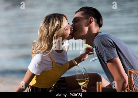 side view of young couple kissing at picnic on river beach in evening Stock Photo