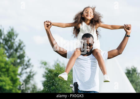 smiling african american police officer with gun holding daughter on shoulders in amusement park Stock Photo