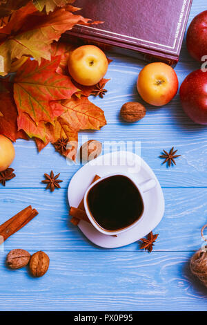 A cup of black hot coffee on a wooden blue table with yellow autumn leaves of a maple book and walnuts. Top view Stock Photo