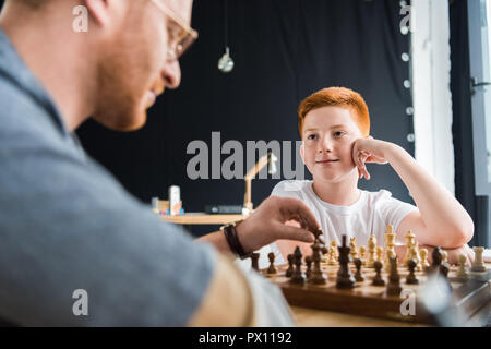 son looking at father playing chess at home Stock Photo