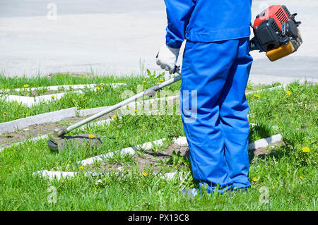 A man in blue working overalls mows the grass with a lawn mower. Close-up Stock Photo
