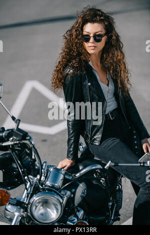 beautiful woman in sunglasses sitting on vintage motorbike on parking Stock Photo