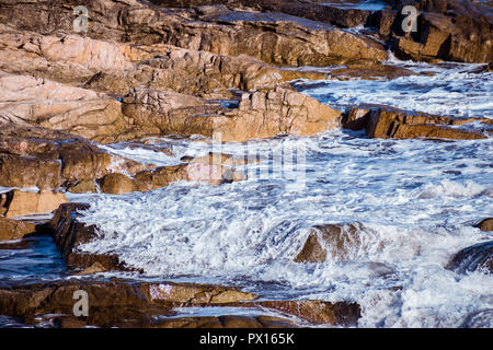 Closeup of a wave gently breaking over shallow rocks on the coast. Stock Photo