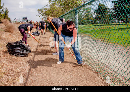 Volunteer women clear and prepare a path next to a chain link fence in a Costa Mesa, CA, park as part of a weekend civic beautification program. Stock Photo