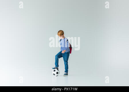 adorable schoolboy with backpack putting leg on fotball ball on white Stock Photo