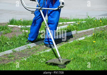 A man in working overalls mows the grass with a lawn mower. Close-up Stock Photo