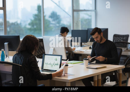 Businessman reviewing the sales graph on laptop and colleagues busy working Stock Photo