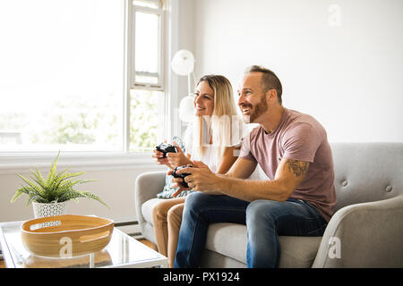 Couple playing video games at home, sitting on sofa Stock Photo