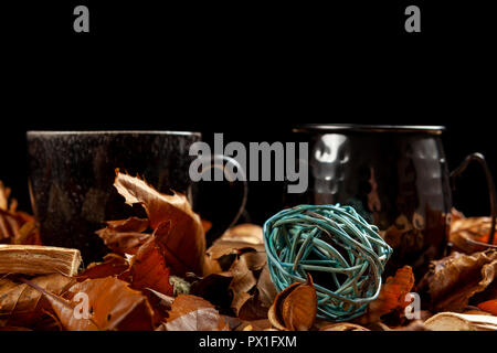 Two rustic looking mugs of coffee amongst fallen autumn leaves against a black background Stock Photo