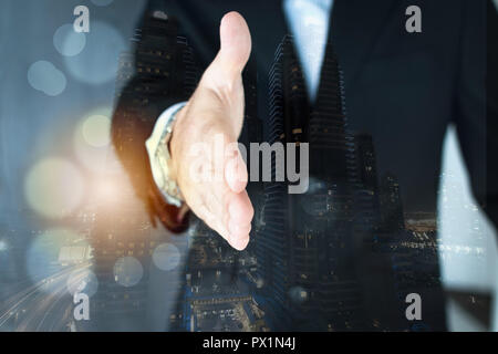 A double exposure shot of a young executive extending his arm for a nahdshake. City scape background Stock Photo