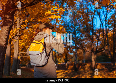 Tourist with backpack walking in autumn forest. Young woman drinking water. Traveller having rest Stock Photo