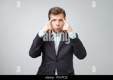 Unhappy puzzled young man pointing at his head with fingers and looking at camera. Isolated on white background. Studio shoot Stock Photo