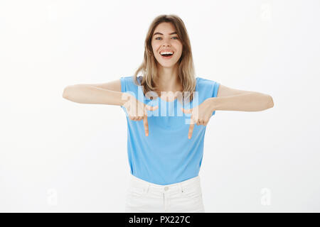 Look down and impress yourself. Portrait of good-looking joyful girlfriend in blue t-shirt, pointing down with index fingers and smiling broadly, showing new shoes to friends during shopping Stock Photo