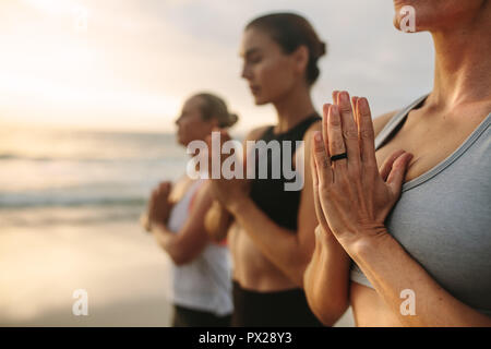 Women practicing yoga on the beach early in the morning. fitness women standing at the beach meditating with joined palms and closed eyes. Stock Photo