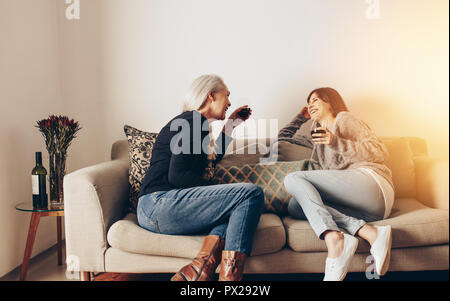 Mother and daughter relaxing on a couch talking while drinking wine. Women enjoying drinks sitting at home on a couch. Stock Photo