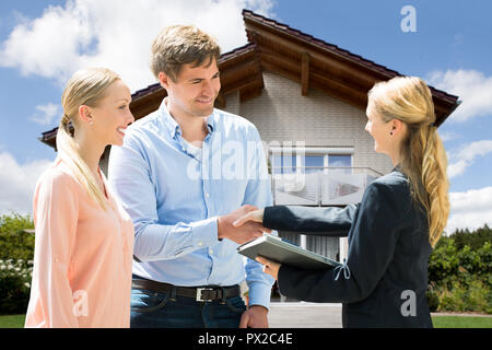 Smiling Female Real Estate Agent Shaking Hand With Young Couple In Front Of House Stock Photo