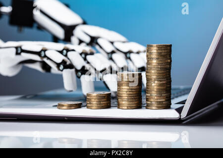 Robotic Hand Working On Laptop With Increasing Stacked Coins On Keypad Stock Photo