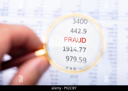 Man's Hand Examining Fraud Word On Financial Report Through Magnifying Glass Stock Photo