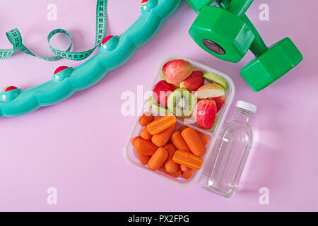Fitness equipment. Healthy food. Concept healthy food and sports lifestyle. Vegetarian lunch. Dumbbell, water, fruits on pink background. Top view. Fl Stock Photo