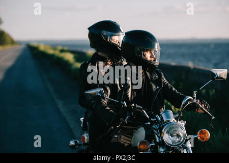 couple of bikers in helmets riding classical motorcycle on country road Stock Photo